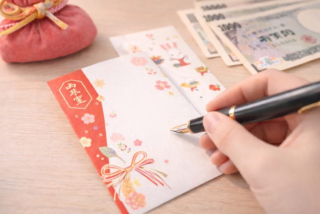 宛名を書き入れる前のお年玉袋に、万年筆を持った手を添えている様子の写真。お年玉の正しい書き方を解説する場面をイメージしたビジュアル。