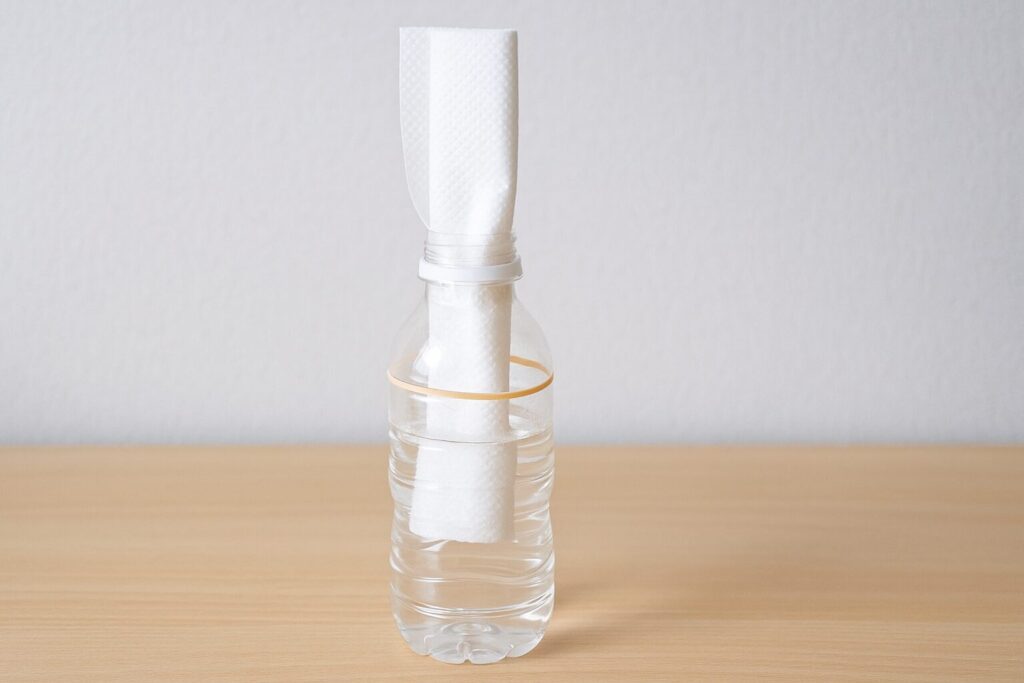 ペットボトルに水を半分入れ、折りたたんだキッチンペーパーを差し込んで輪ゴムで固定した自作加湿器の写真。紙が水を吸い上げて蒸発する仕組みを利用した簡単な加湿方法。